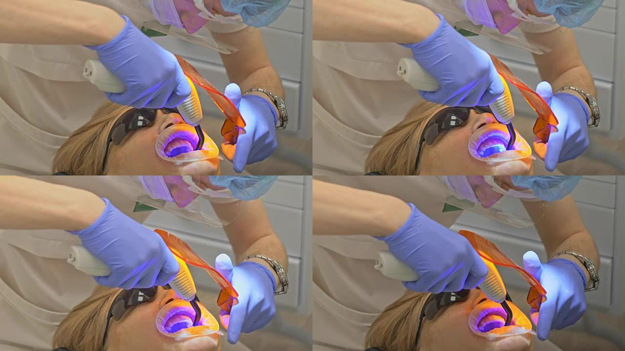 牙医正在现代牙科诊所治疗病人。正畸医生与助手一起工作。患者用蓝色激光牙齿消毒。橙色玻璃快门用于保护眼