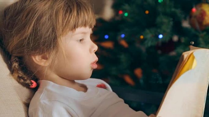 Small girl reading a book in front of Christmas tr