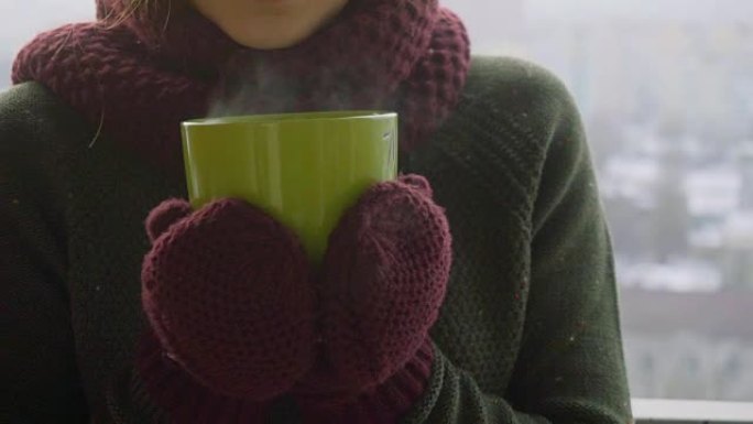 女人在冬天的早晨从绿杯中喝热茶或咖啡