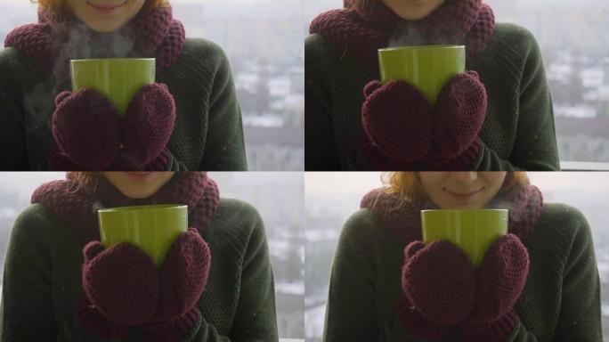 女人在冬天的早晨从绿杯中喝热茶或咖啡