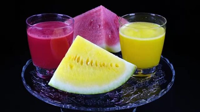 红色和黄色的西瓜金字塔和几杯鲜榨果汁，在时钟关闭的黑色背景上旋转。
