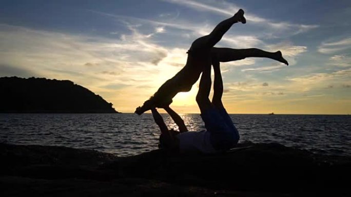 夫妻在日落时在海边的岩石上进行Acro瑜伽。