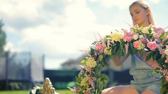 儿童课外活动弗洛里斯蒂克接待装饰课程 -- 漂亮的女模特金发微笑的女孩在户外翡翠草地上用花朵制作花卉