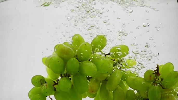 一束绿色葡萄在慢动作中带着气泡落入水中。白色背景上的浆果。