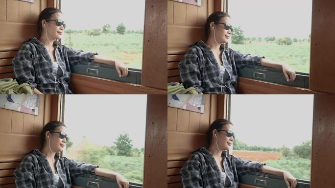 4K.亚洲妇女戴着太阳镜，从火车上的火车窗外看耳机听音乐，从曼谷开始，前往泰国的北碧府。享受老式火车
