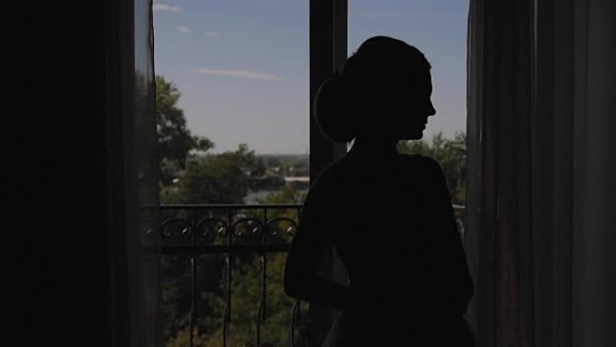 一名年轻女子走近窗户，打开阳台，享受着。等待婚礼的早晨新娘