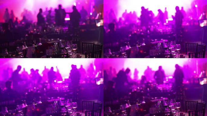 在餐厅或夜总会举行的青年聚会，在跳舞的人的剪影，舞台灯光和紫色填充的背景下摆满酒精和食物的宴会桌