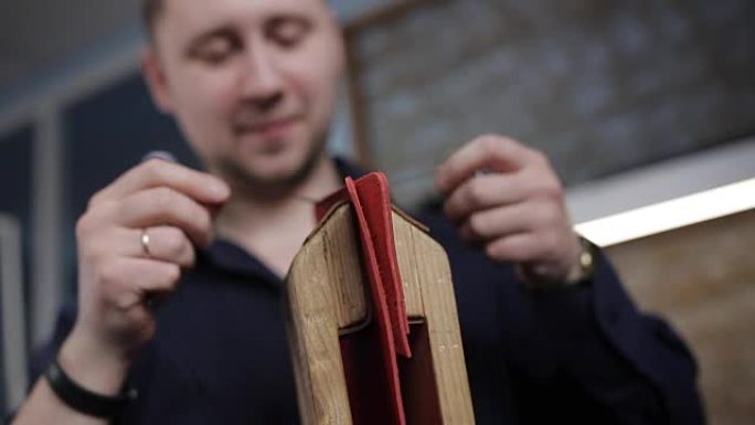 男子在皮革车间用针用自己的手制作了一个棕色皮革钱包，特写