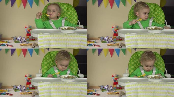婴儿坐在高脚椅上，用勺子，盘子和玩具等婴儿