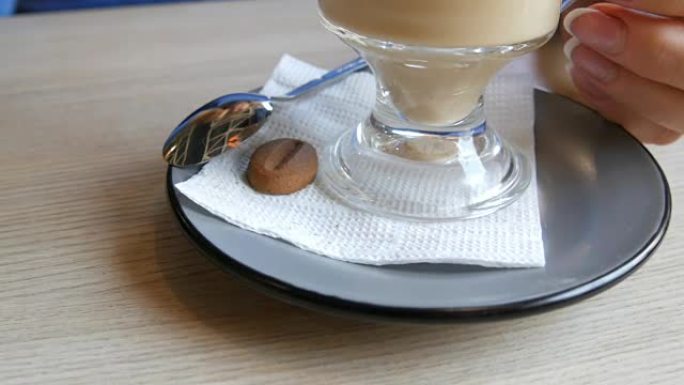 女人在咖啡馆里转动一个碟子和一杯拿铁咖啡，碟子上放着一个咖啡豆形式的饼干
