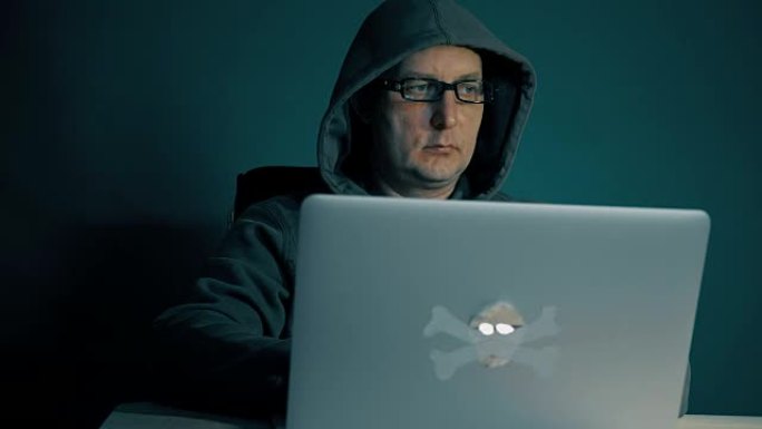 成年男子在电脑上浏览互联网。男人深夜坐在桌子旁，手提电脑。他的时尚眼镜上的屏幕上的耀斑。电脑屏幕反射