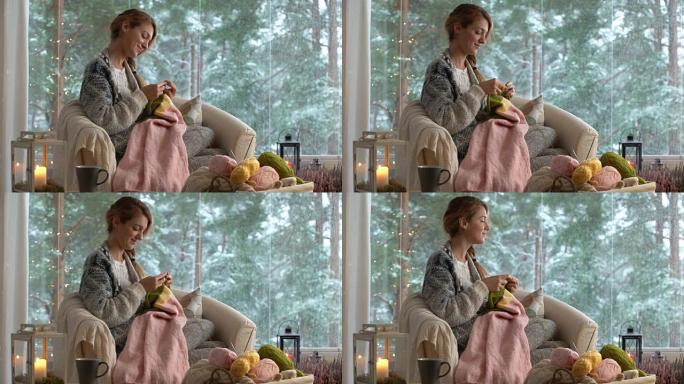 年轻女子在客厅编织保暖羊毛衫，抵御外面的雪景