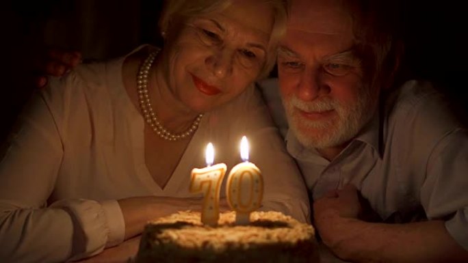 充满爱心的高级夫妇庆祝70周年纪念日，晚上在家吃蛋糕。吹灭蜡烛