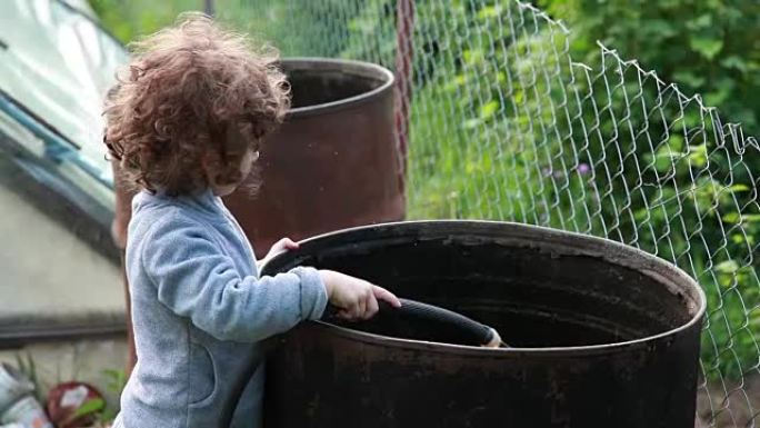 儿童将水从软管倒入大金属桶