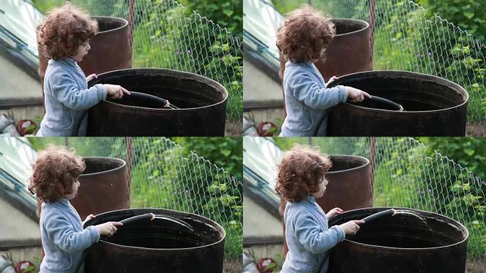 儿童将水从软管倒入大金属桶