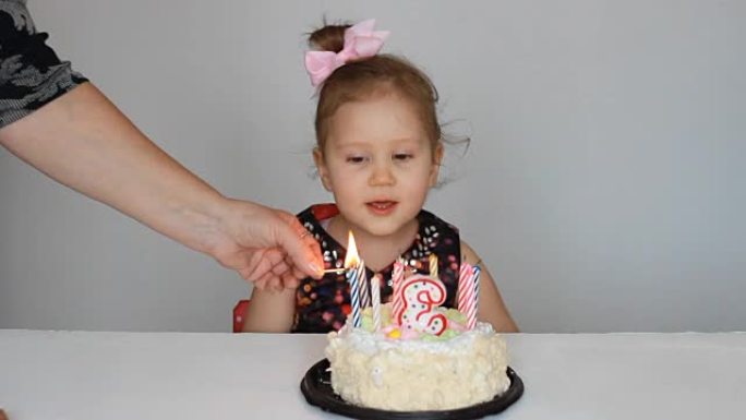 小女孩在派对上观看节日蛋糕上的蜡烛火焰。有趣的快乐孩子。儿童假期的概念。3年