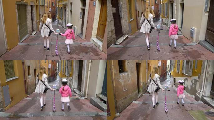 母亲和女儿带着踏板车沿着古老的欧洲城市的狭窄街道行走