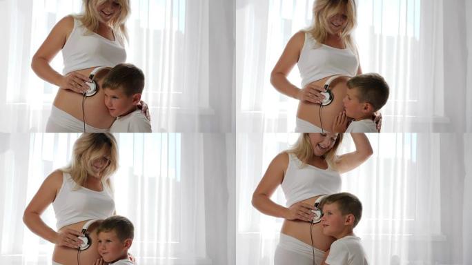 男孩听着母亲怀孕的肚子，女人拿着耳机在裸露的大肚子上微笑
