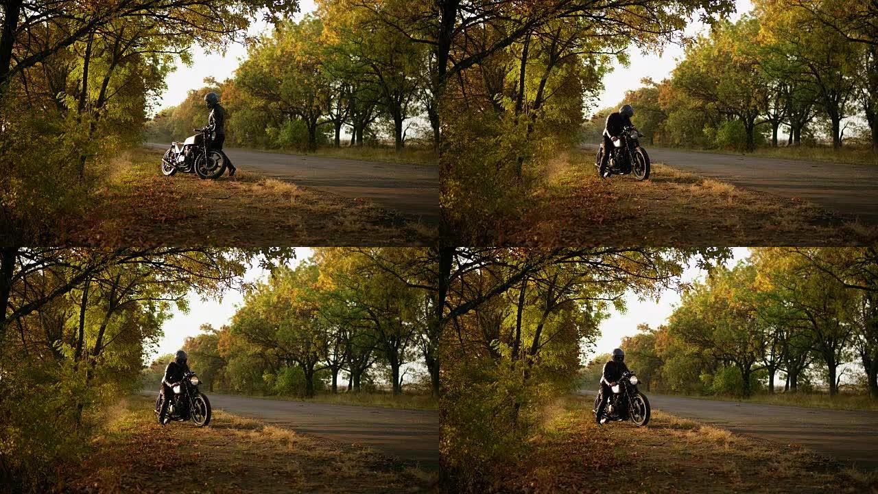 穿着头盔和皮夹克的面目全非的时尚男人在秋天的阳光明媚的日子里站在路边时骑着自行车启动引擎