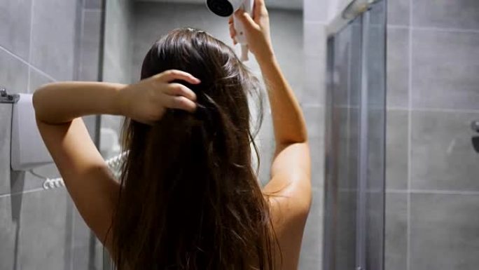 护发女孩手持电动吹风机，在酒店房间的浴室吹湿头发