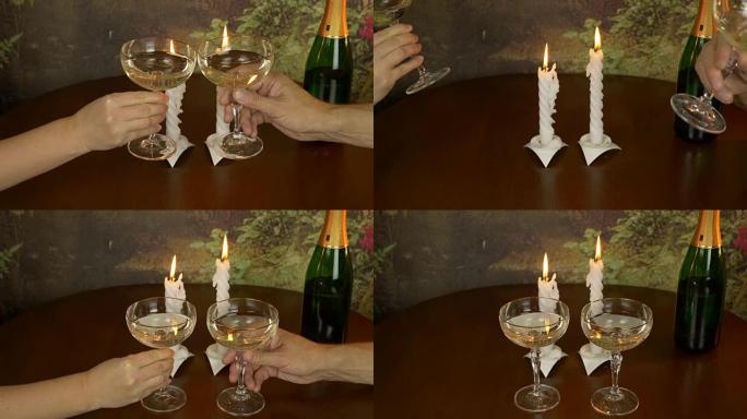男人和女人的两只手拿着香槟和喝酒。桌子上有两支蜡烛和一瓶香槟。两个人的浪漫晚餐。