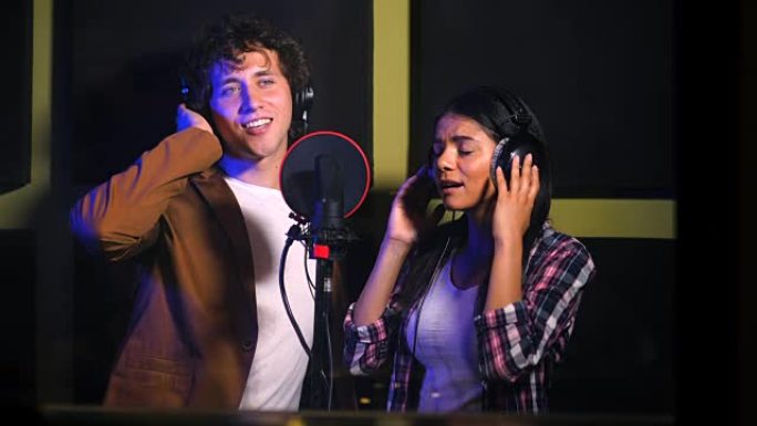 两位年轻歌手在唱片工作室表演他们的歌曲。专业音乐家二重唱录制新专辑CD。美丽的夫妇一起工作。慢动作