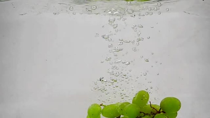 成熟的绿色葡萄落入带有气泡的纯净水中。慢动作白色背景上的葡萄浆果。