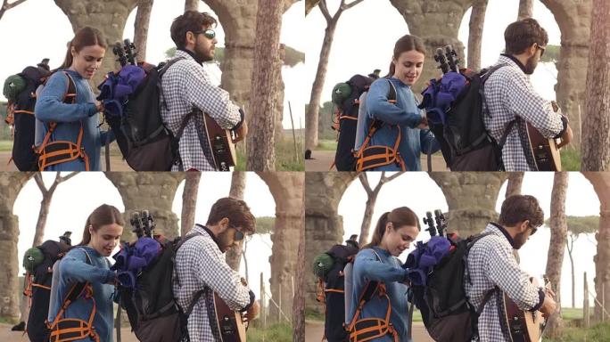 年轻夫妇背包客游客在日出时用吉他和睡袋慢动作steadycam搜索罗马parco degli acq