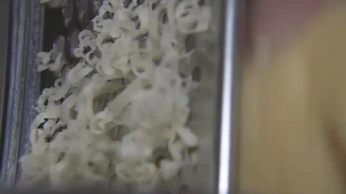 用金属刨丝器手工磨碎黄色奶酪。特写。