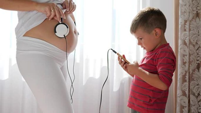 孕妇通过耳机给肚子里的婴儿播放音乐，手机进入站在旁边的小男孩的手中