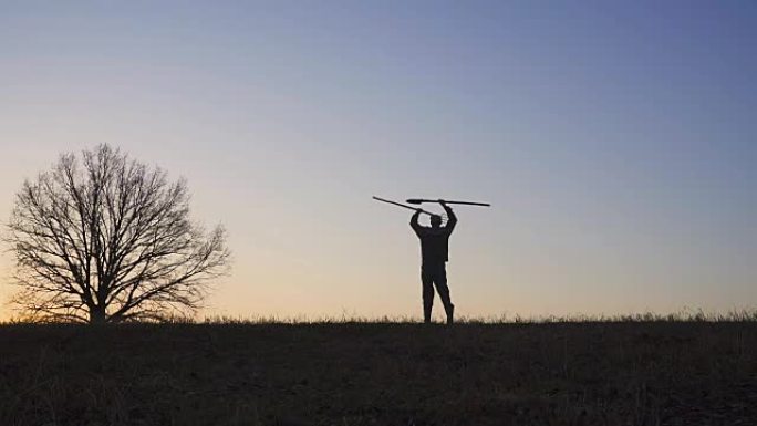 一个满意的农民用铲子和干草叉挥舞着双手。野外日落或日出的轮廓。