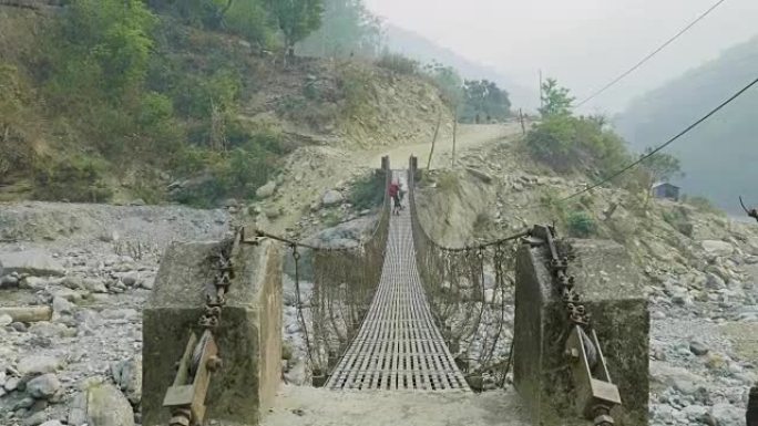 两名背包客沿着尼泊尔的一座悬挂式金属桥走。