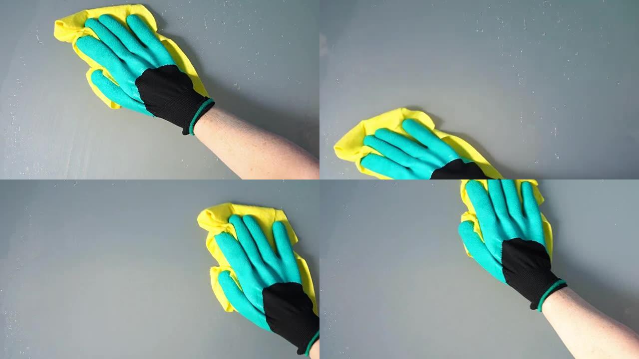 女人的手戴着绿色手套，用黄色抹布清洁湿磨砂玻璃