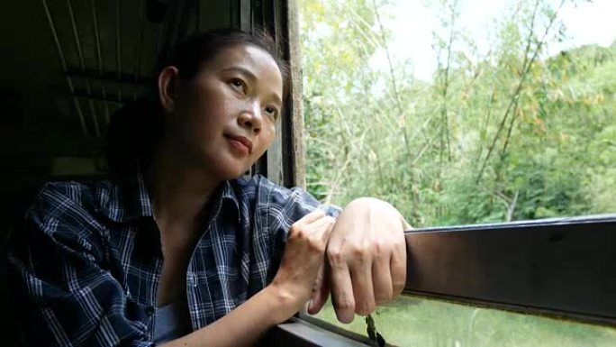 4K.亚洲妇女乘火车旅行，从火车上的火车窗外望去，从曼谷开始，去泰国的北碧府。享受老式火车的交通