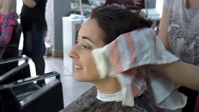 女美发师毛巾在美容院擦拭一个美丽女孩的湿头发。头发护理。特写。