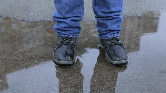 一个穿着冬靴的孩子在水坑里跳