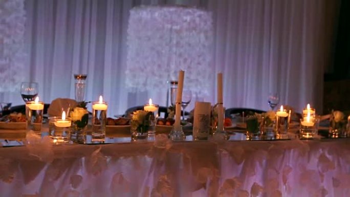 婚礼宴会厅内部细节，餐厅装饰餐桌。蜡烛和白色花瓣装饰，玫瑰花在装满水的玻璃花瓶中
