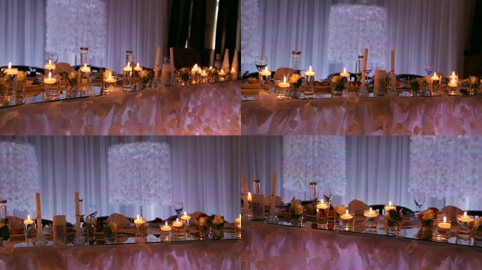 婚礼宴会厅内部细节，餐厅装饰餐桌。蜡烛和白色花瓣装饰，玫瑰花在装满水的玻璃花瓶中