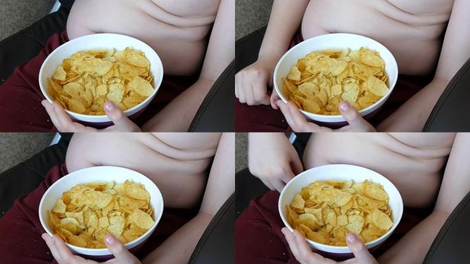 身体上有脂肪褶皱的胖少年正在吃薯片。不健康食品，快餐。孩子的营养问题