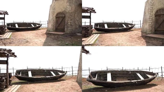 旧的破旧的黑色木船，在俄罗斯哥萨克村有一个单层的房子，一个水井和一个小山。视频。一艘长满鲜花的老船。