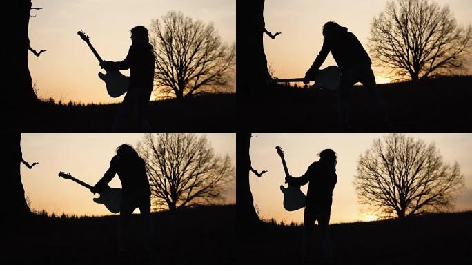人在日落时在树附近的田野里弹电吉他，唱一首抒情歌。剪影