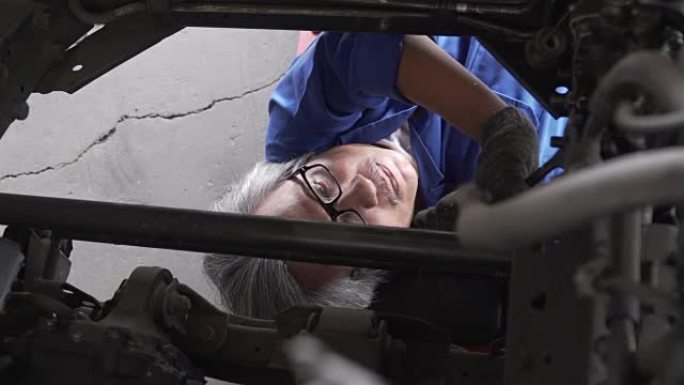 多莉从顶视图拍摄: 亚洲高级汽车修理工在车辆下工作
