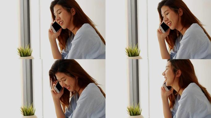 漂亮的年轻女子亚洲打电话给家里卧室窗户旁边的电话。