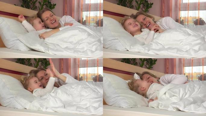 顽皮的笑女孩躺在床上的母亲附近