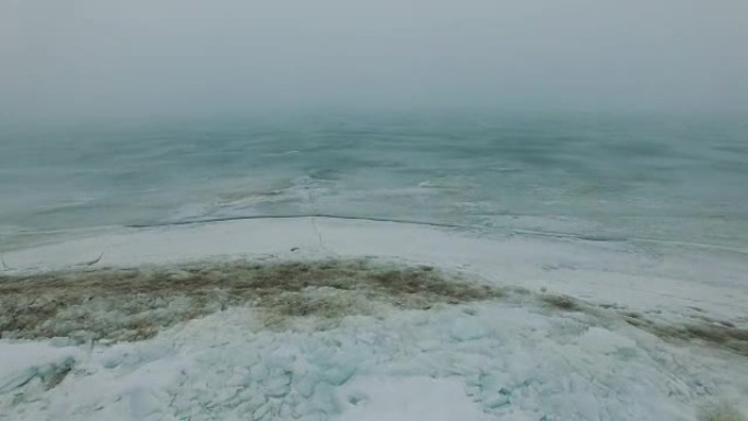 在雾蒙蒙的寒冷冬季，在冰冻的海上海岸线上飞行，冰裂