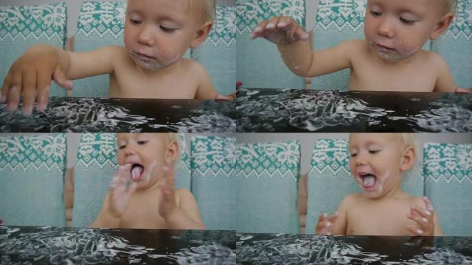 宝宝吃酸奶弄得一团糟。特写镜头的白人小女孩涂抹酸奶在黑色的玻璃桌上，并拍她的手。