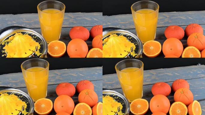 橘子，橘子，一杯橙汁和蓝色木制背景上的手动柑橘squezeer。橘子切成两半