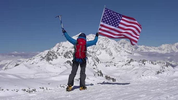 站在白雪皑皑的山顶上的登山者放弃了美利坚合众国的国旗。