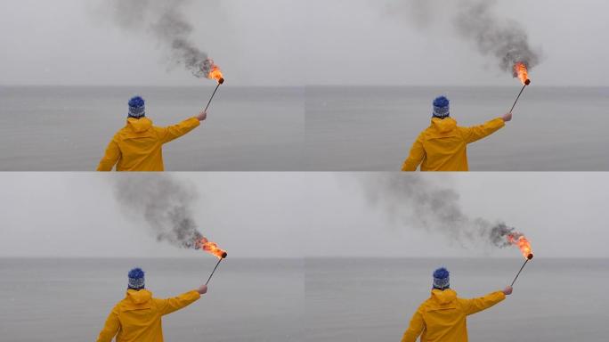 在冰冻的大海背景下，穿着黄色外套的火把的人的后视图。雪落在前景