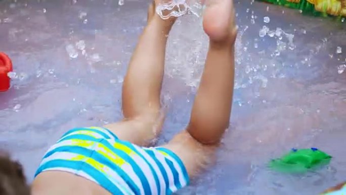 脚的特写。一个四岁的男孩躺在儿童充气池中，溅水，溅水散落。附近的漂浮玩具